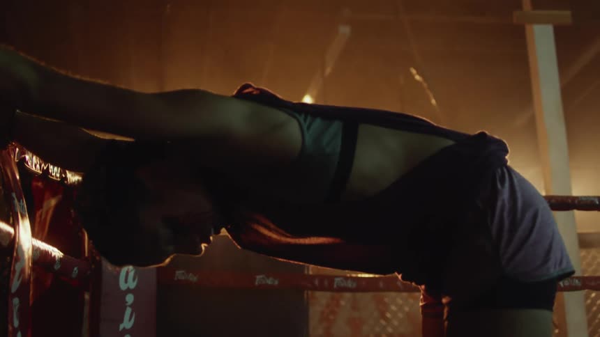 Woman wearing boxing gloves bends with her hands on boxing ring rope