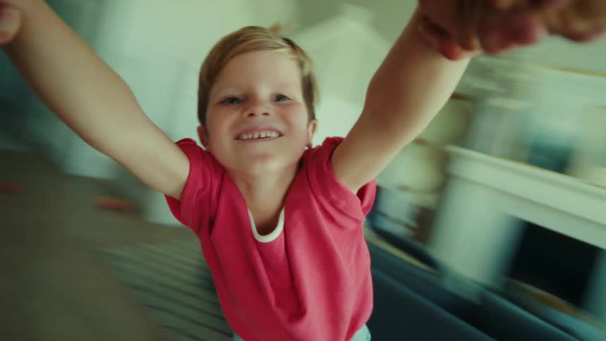 A joyful young boy laughs as an adult spins him around during a playful moment at home