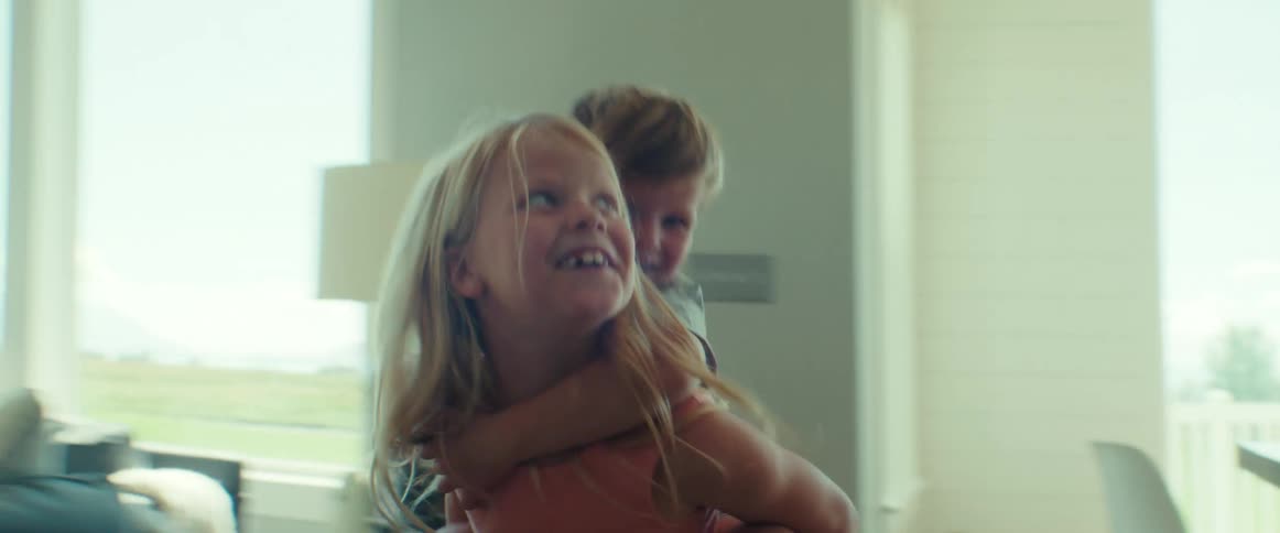 Two siblings laugh and play as an older child gives a piggyback ride during a joyful moment at home