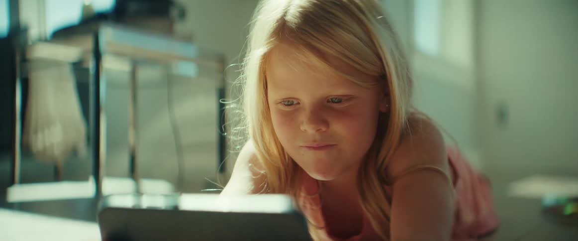 Blue eyed blonde girl lies down and plays on smartphone smiling