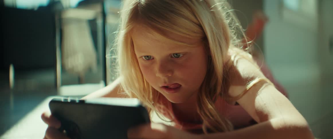 Blue eyed blonde girl lies down and plays on smartphone smiling