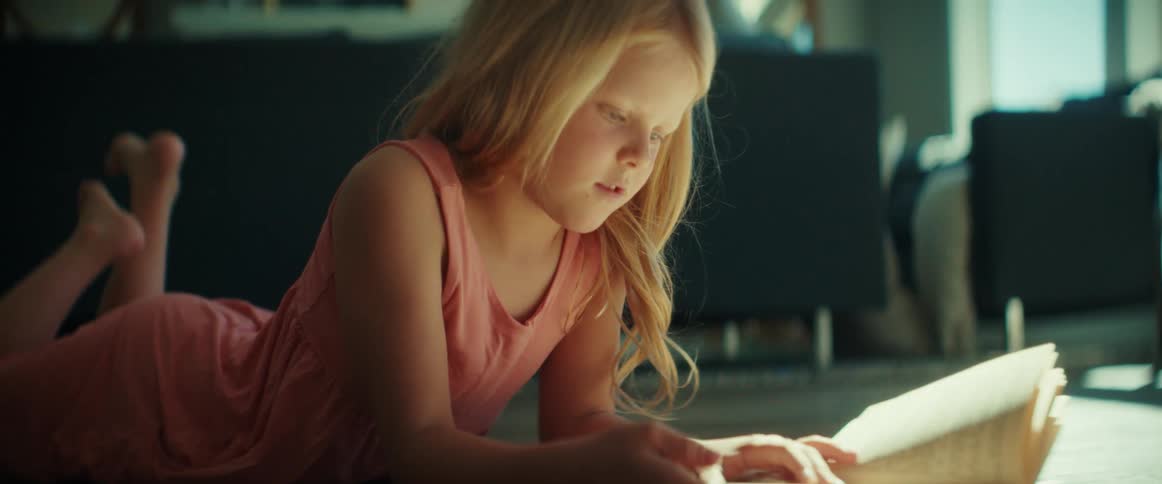 A little girl is lying on the floor looking at a book and turning the pages