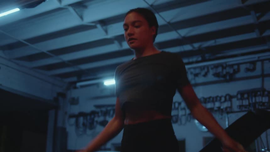 A woman exercises using a jump rope in a dimly lit garage