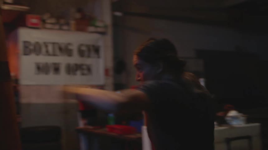 Young female boxer practices with a punching bag on the back of a gym