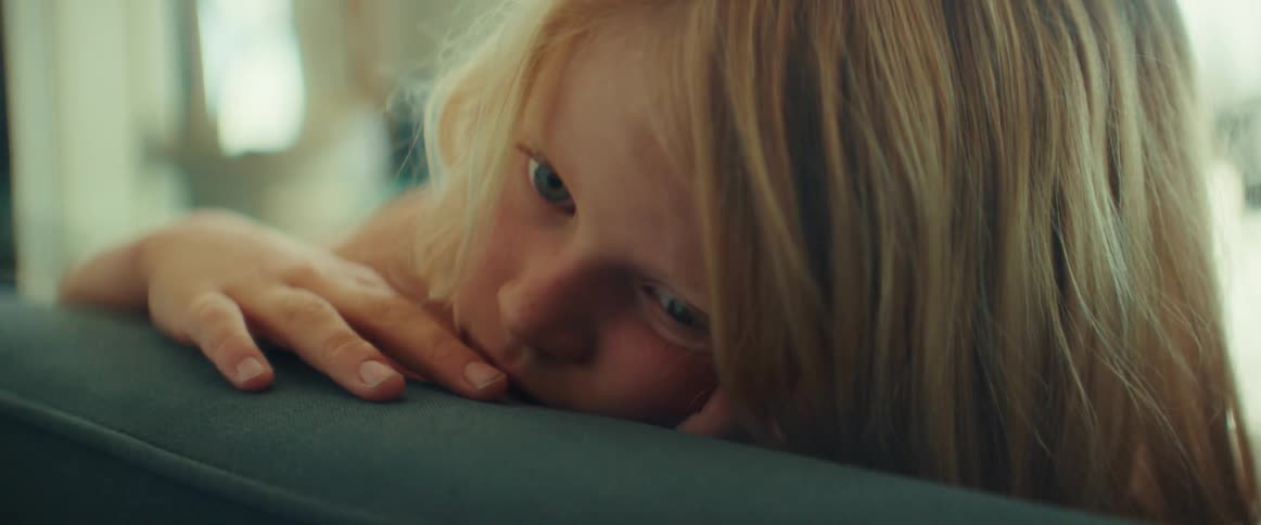 Blue eyed blond toddler lies on couch looking into space