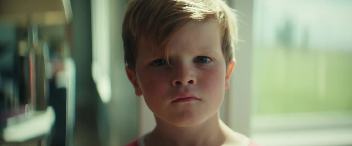 Boy standing near window stares with a set jaw