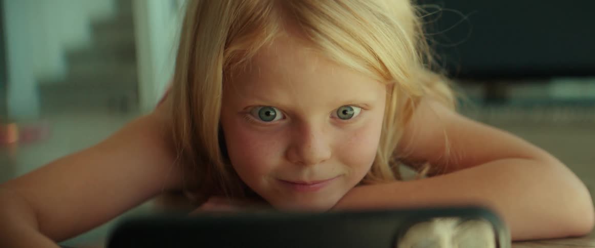 Blue eyed blonde girl watches smartphone smiling