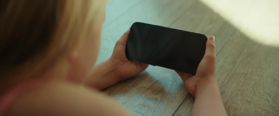 A girl lying on the floor talking to the smartphone held landscape in her hands