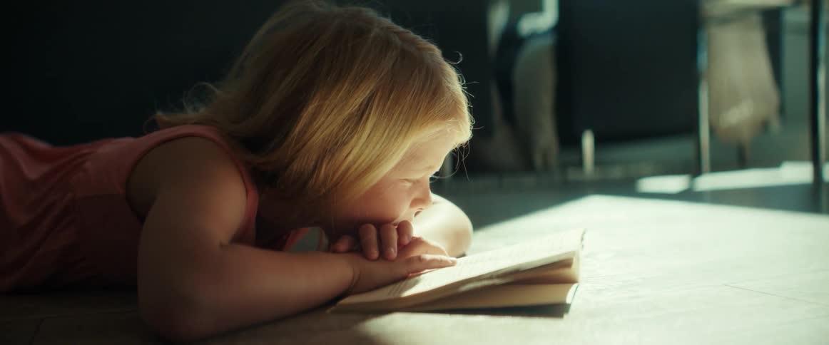 Sunlight shines on a little girl lying on the floor reading a book