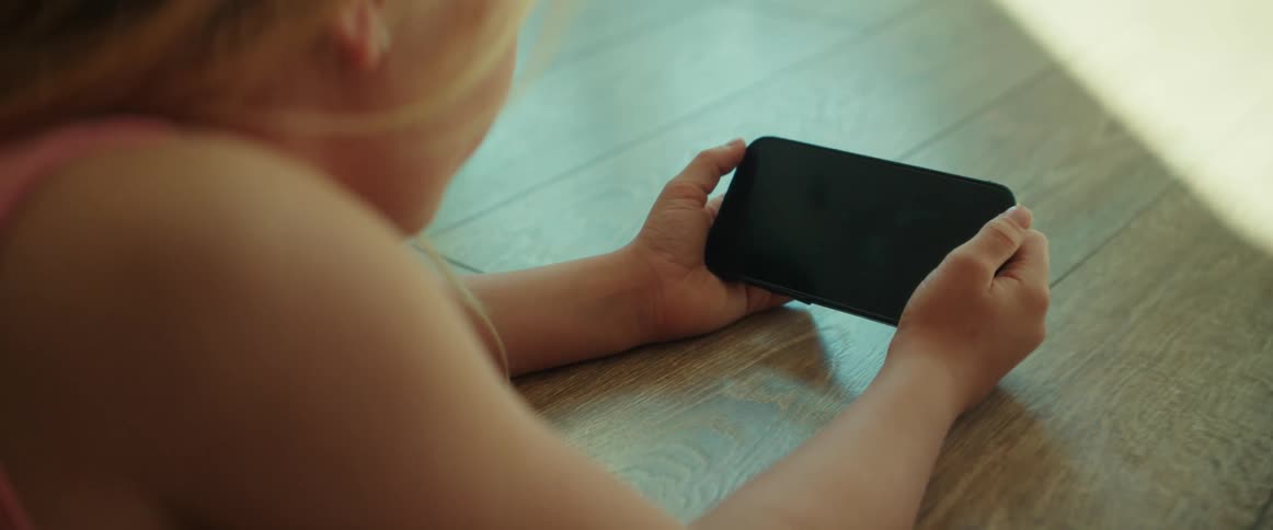 Young girl holding a smartphone on her hands while resting on the floor at home