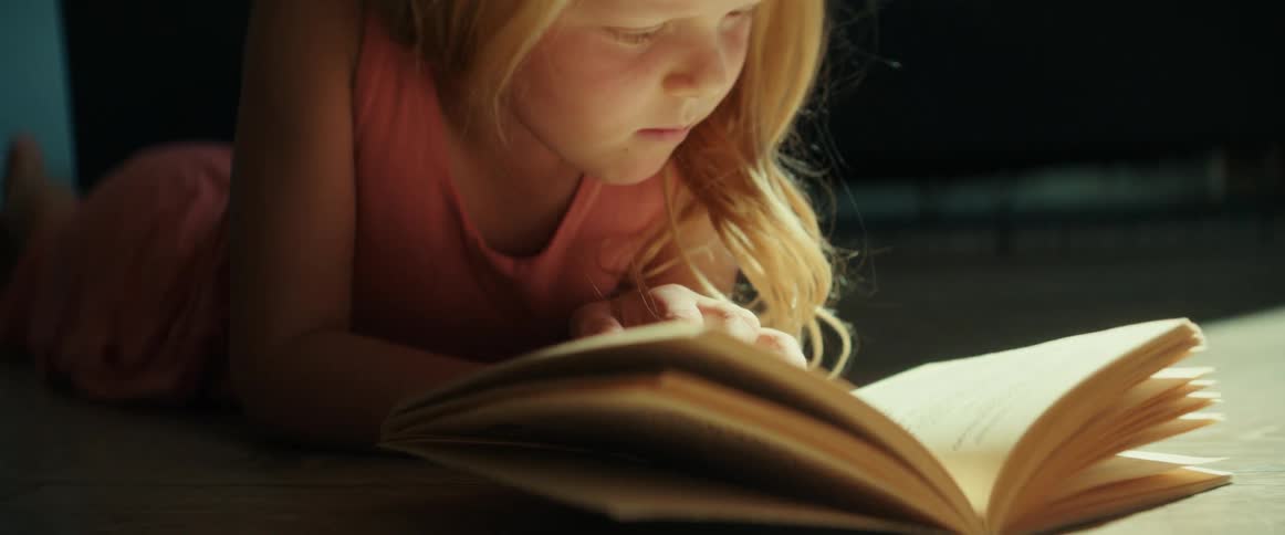 A little girl is lying on the floor reading a book