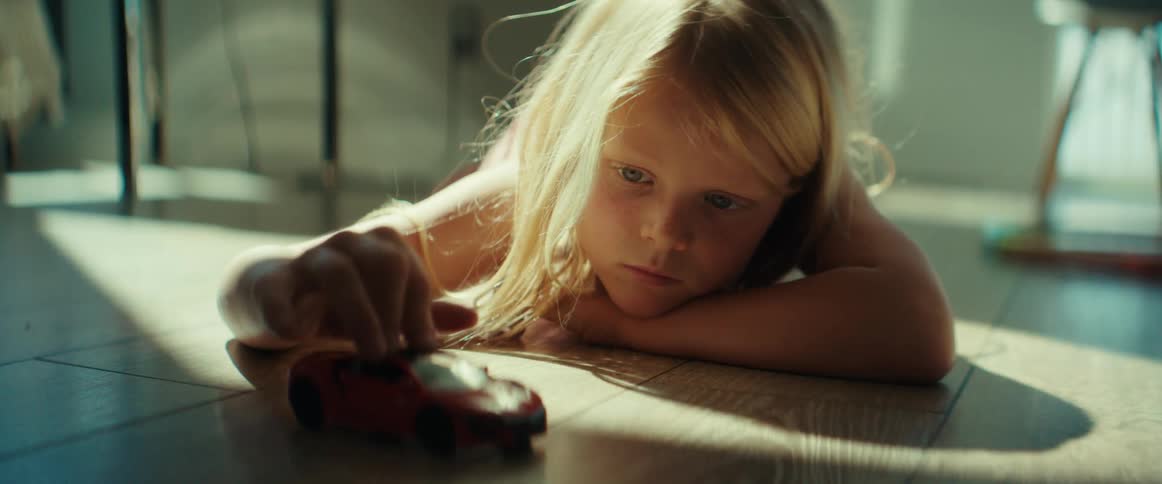 A girl lies on the floor and plays with a toy car