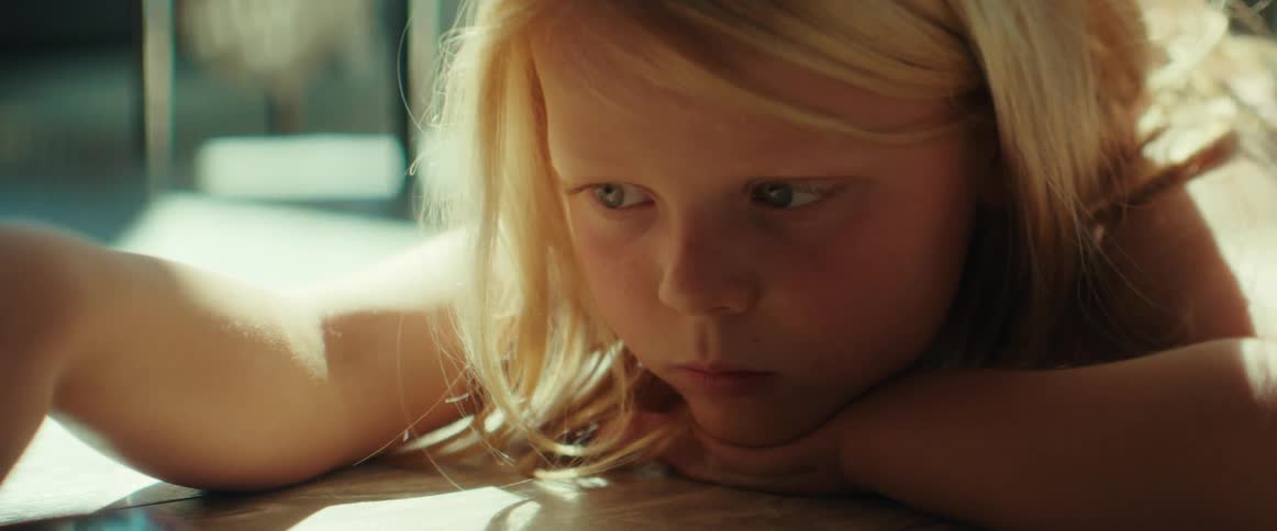 A bored little girl plays with a toy car while lying on the floor