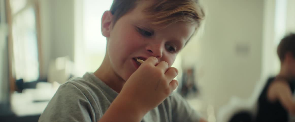 Young boy sitting in the kitchen at home eating with his hands