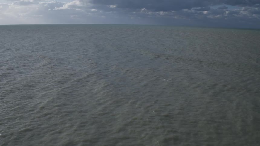 Waves break against a white cliff as the camera pans out to sea and the horizon