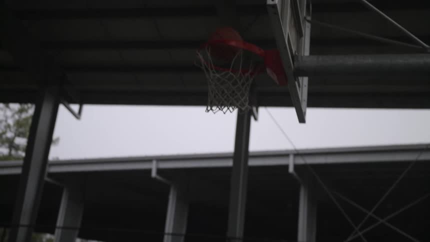 A teenage boy runs across the basketball court and leaps into the air to put the ball through the hoop