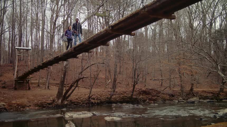 Three people are walking on a bridge in a wooded area