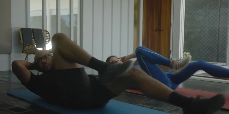 A man and a woman are lying side by side on mats on the floor doing exercises