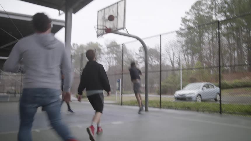 A group of teenage boys are playing basketball at a park