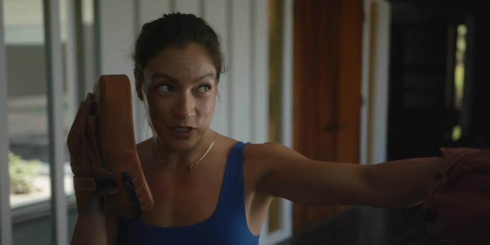 Female boxer with a ponytail blue sports bra and brown boxing pads shows how to punch in the gym