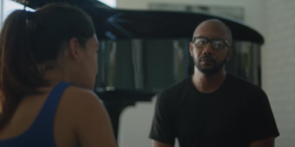 A man and a woman are sitting down inside a room talking and he nods his head