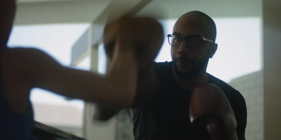 A woman is wearing punch mitts as a man is punching them giving her boxing training
