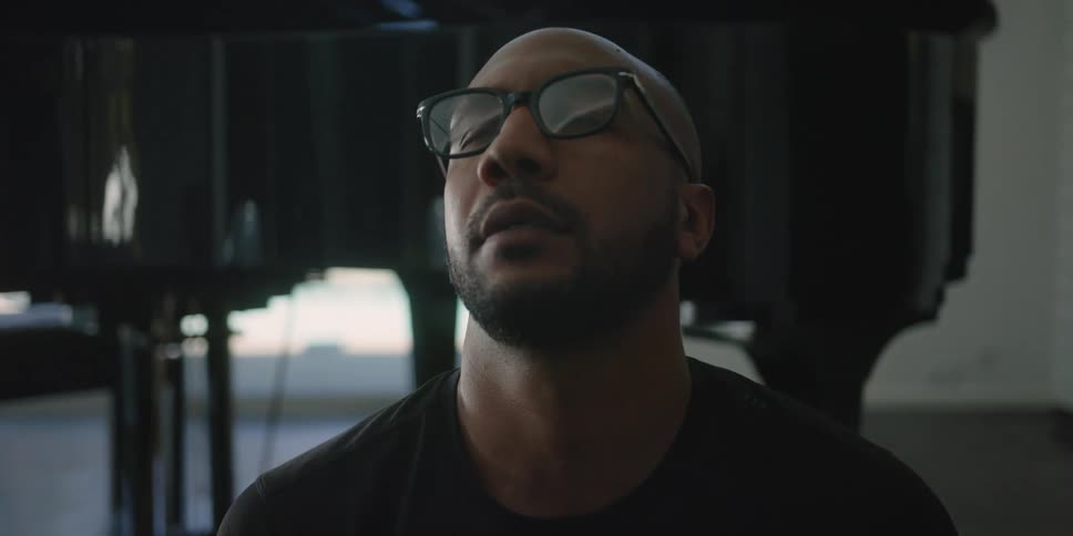 A man is sitting indoors and wearing glasses