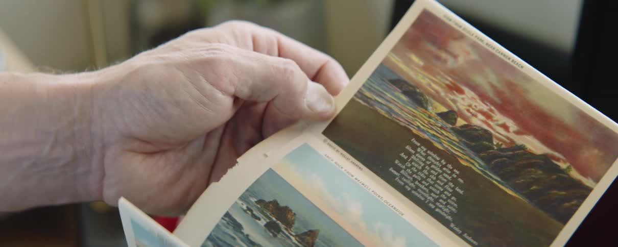 Close up of the hands of an elderly man unfolding a collection of vintage postcards