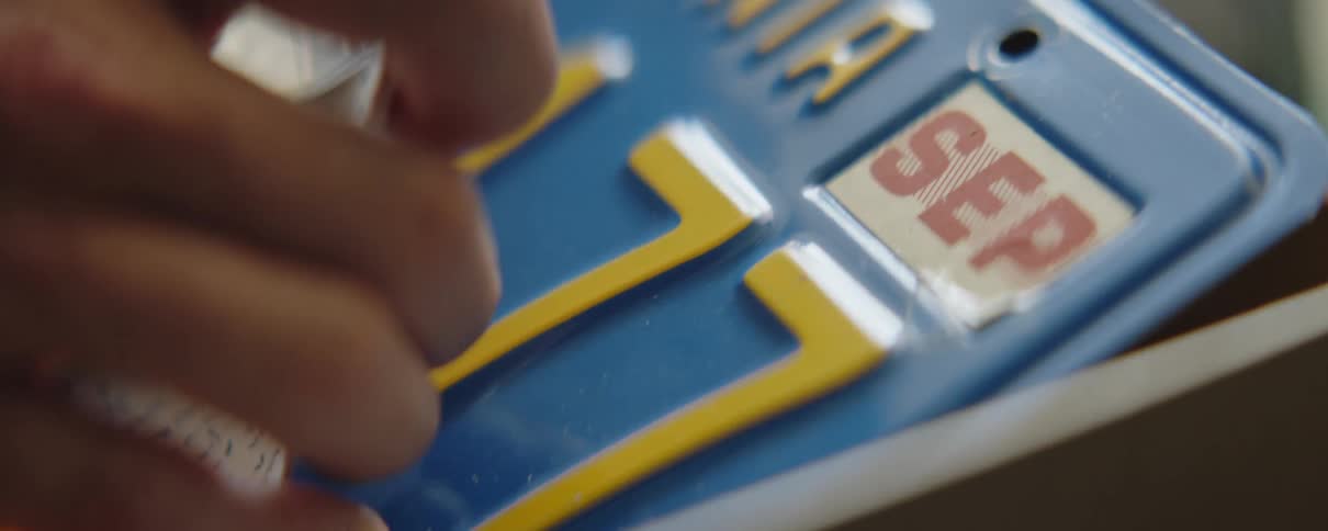 Close up of a man lifting a piece of paper up off a license plate