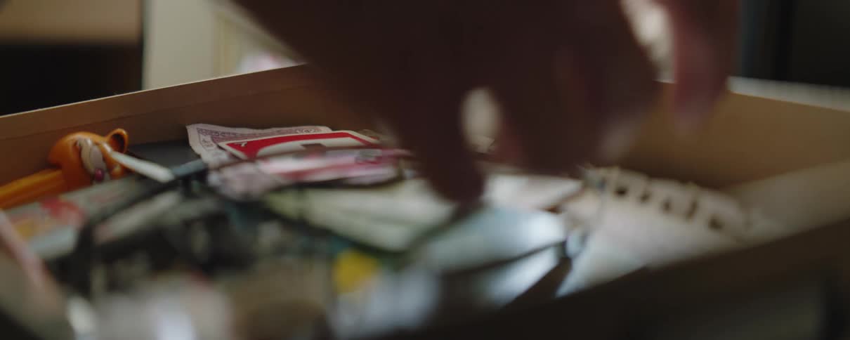 A man at home sifts through of drawer of items in front of a portrait of a little girl
