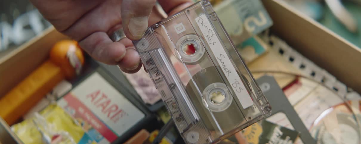 A man is holding a cassette tape over a box filled with things from the eighties