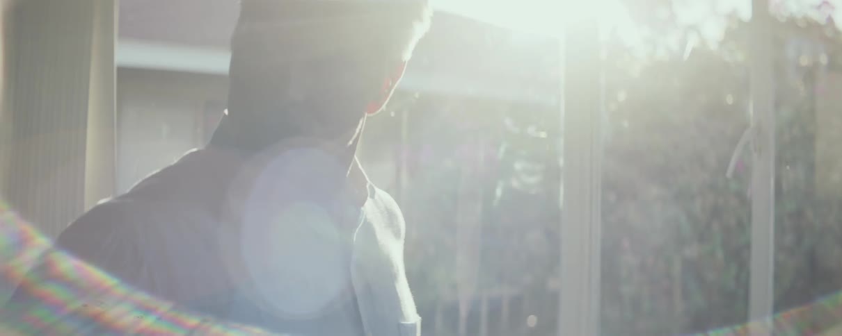 A man is standing inside near windows and the sun shines brightly as he turns around