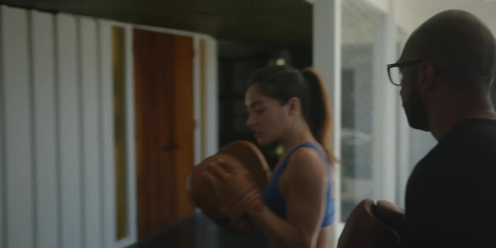 A man and woman are standing together wearing boxing gloves and she is teaching him how to box