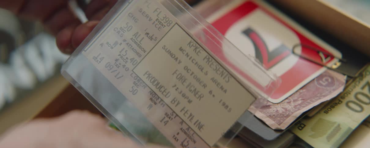 A man flips through a box with papers and then runs his finger over a ticket in a plastic pocket
