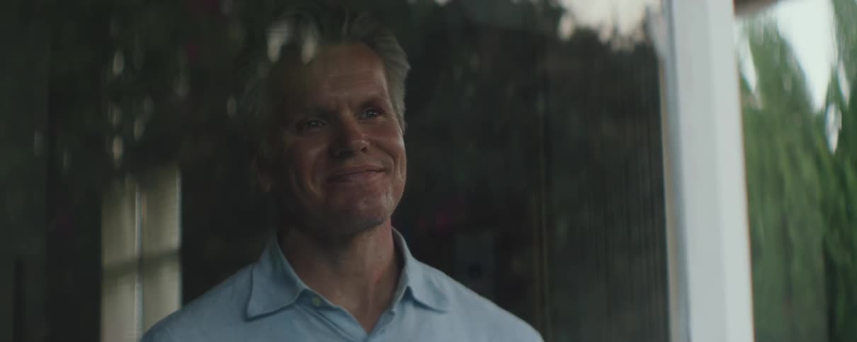 Close up of the face of a mature man standing behind a window smiling