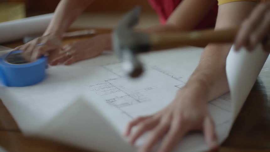 Two people unroll a floor plan on a table