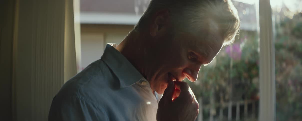A man at home looks down and runs his fingers over his mouth as he thinks