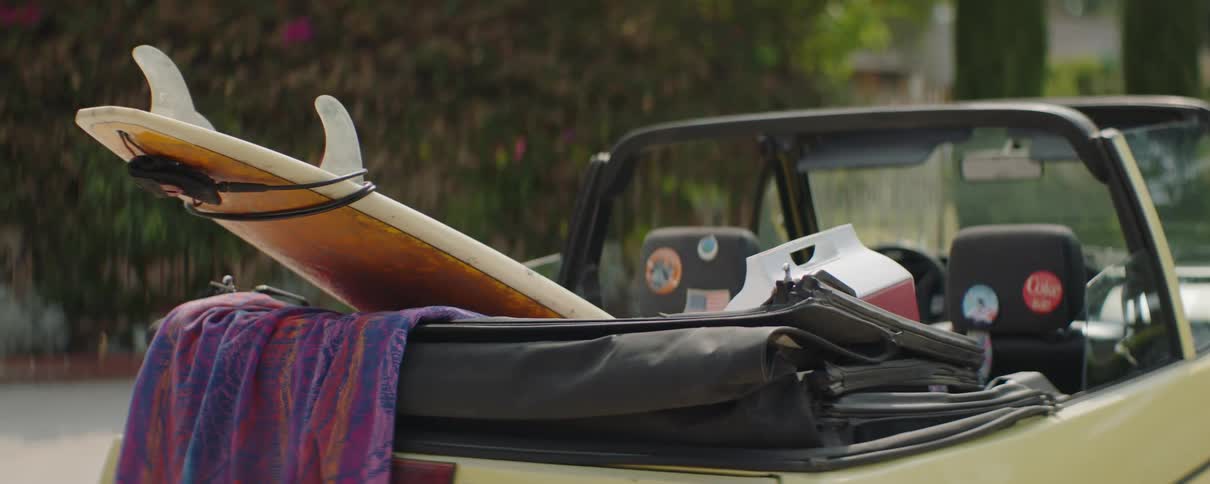 A surf board in the back of a convertible