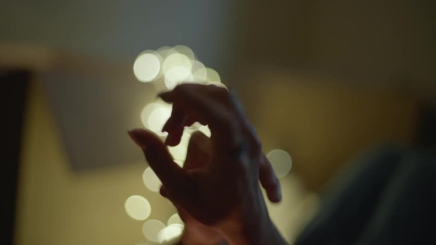 Close up of the wiggling fingers of a female hand on a room in front of christmas lights