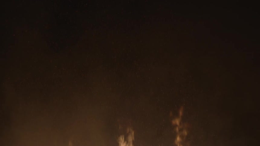 A fence-like structure made of wood slats burns at night