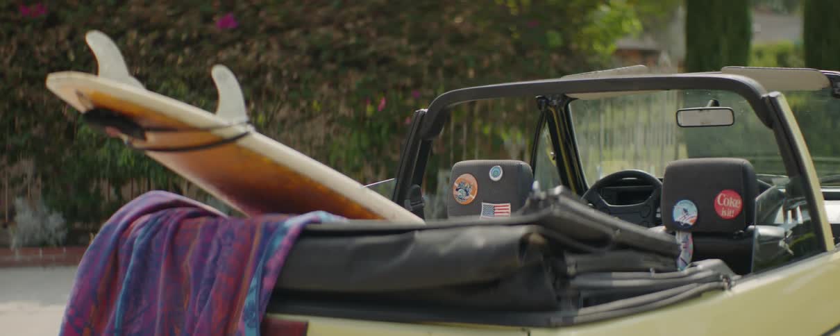 A surfboard is hanging out of the parked car