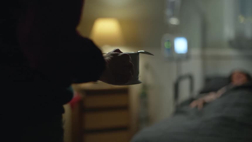 Man carries mug and spoon toward bed of patient at home