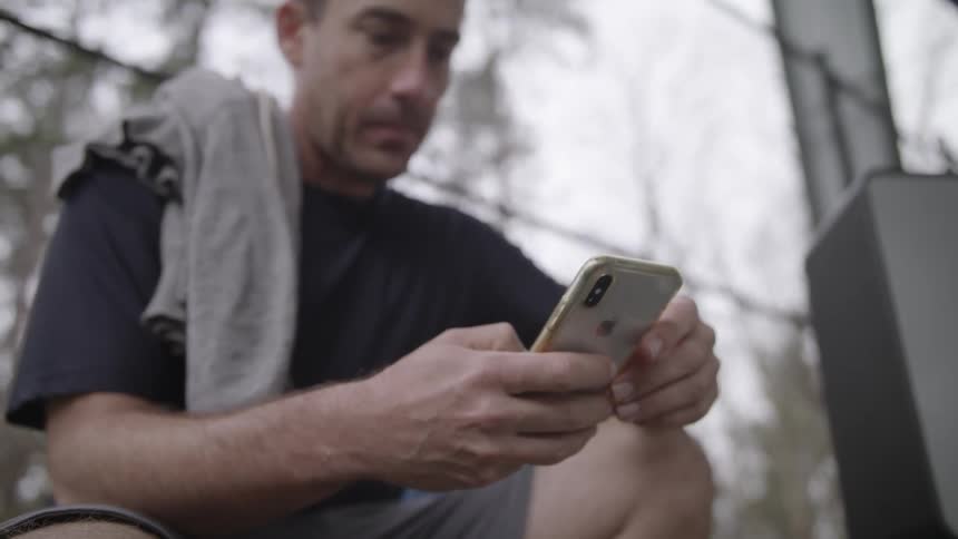 Man sits outdoors with a shirt thrown over his shoulder and swiping on smartphone