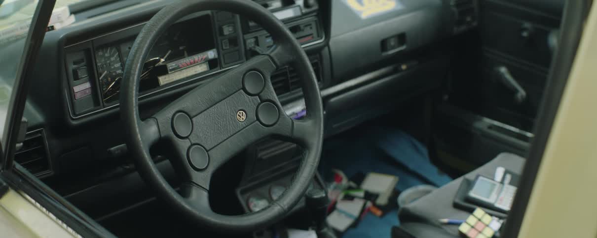 Inside of an automobile vhs tapes are sitting near the speedometer and a calculator and rubiks cube are sitting on the passenger seat