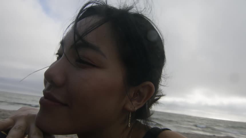 Close up of the face of a happy relaxed woman laying on the sand beach at evening next to the ocean