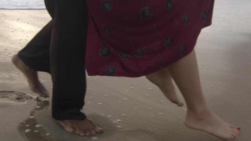 Man carries woman before putting her down on beach near surf