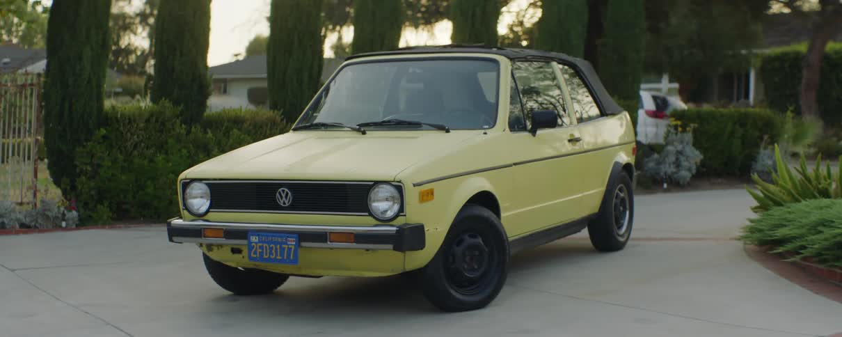 Yellow compact car sits parked in curved driveway as traffic passes on street in the background