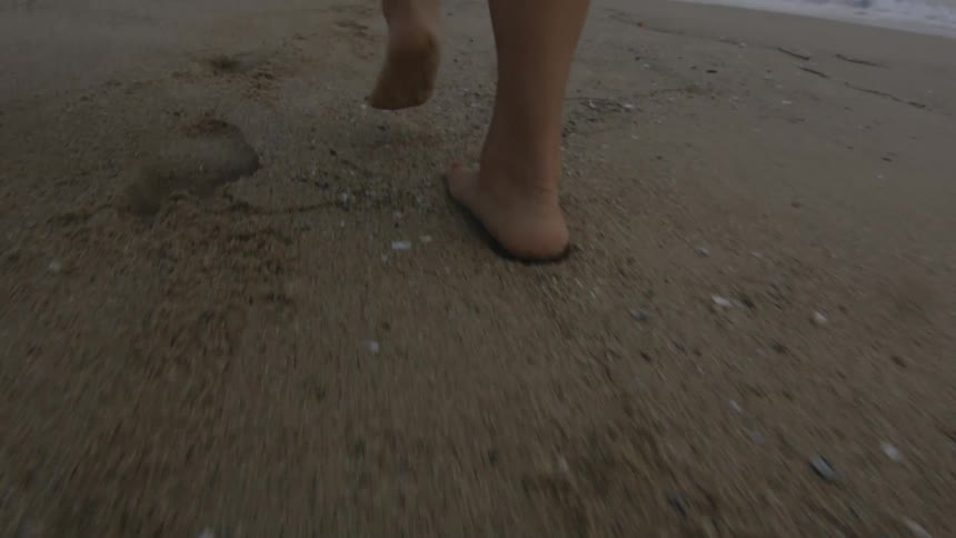 The feet of a woman as she walks on a beach