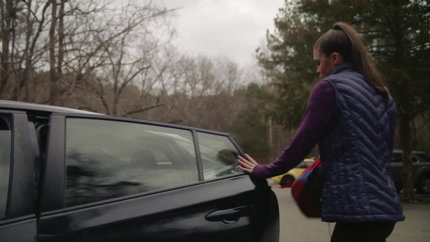 Woman exits a black car parked outdoors and walks away with her backpack