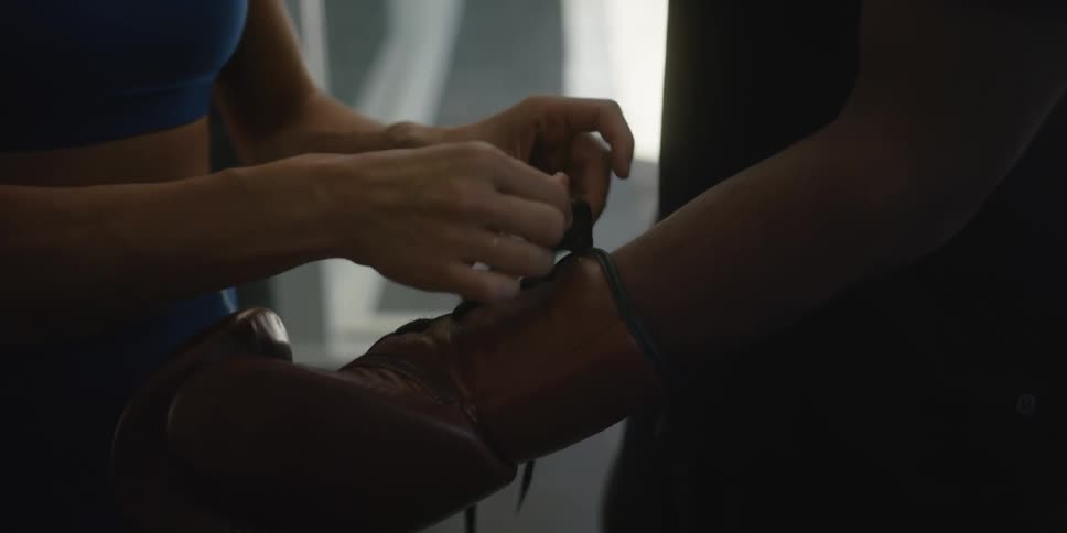 Woman ties the laces on the boxing gloves of a man